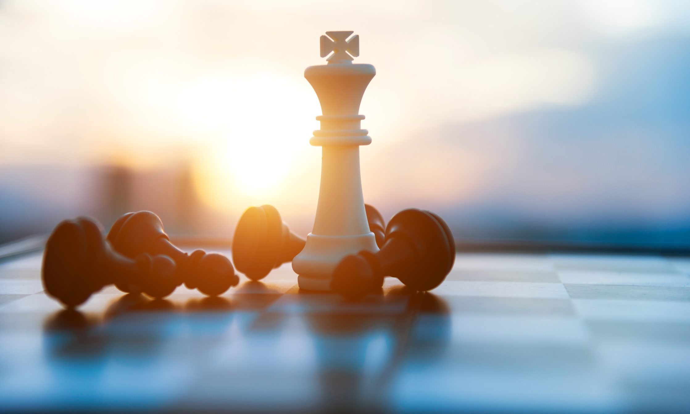 A white king chess piece stands upright with fallen black pieces around it on a chessboard.