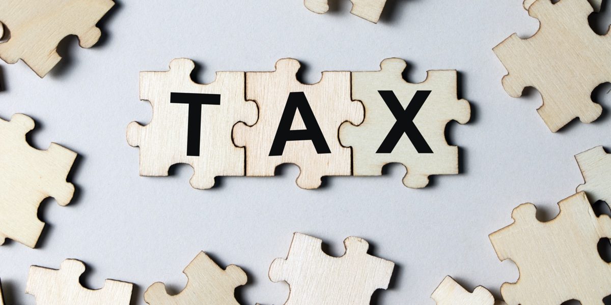 Wooden puzzle pieces with the word 'TAX' in the center on a gray background.