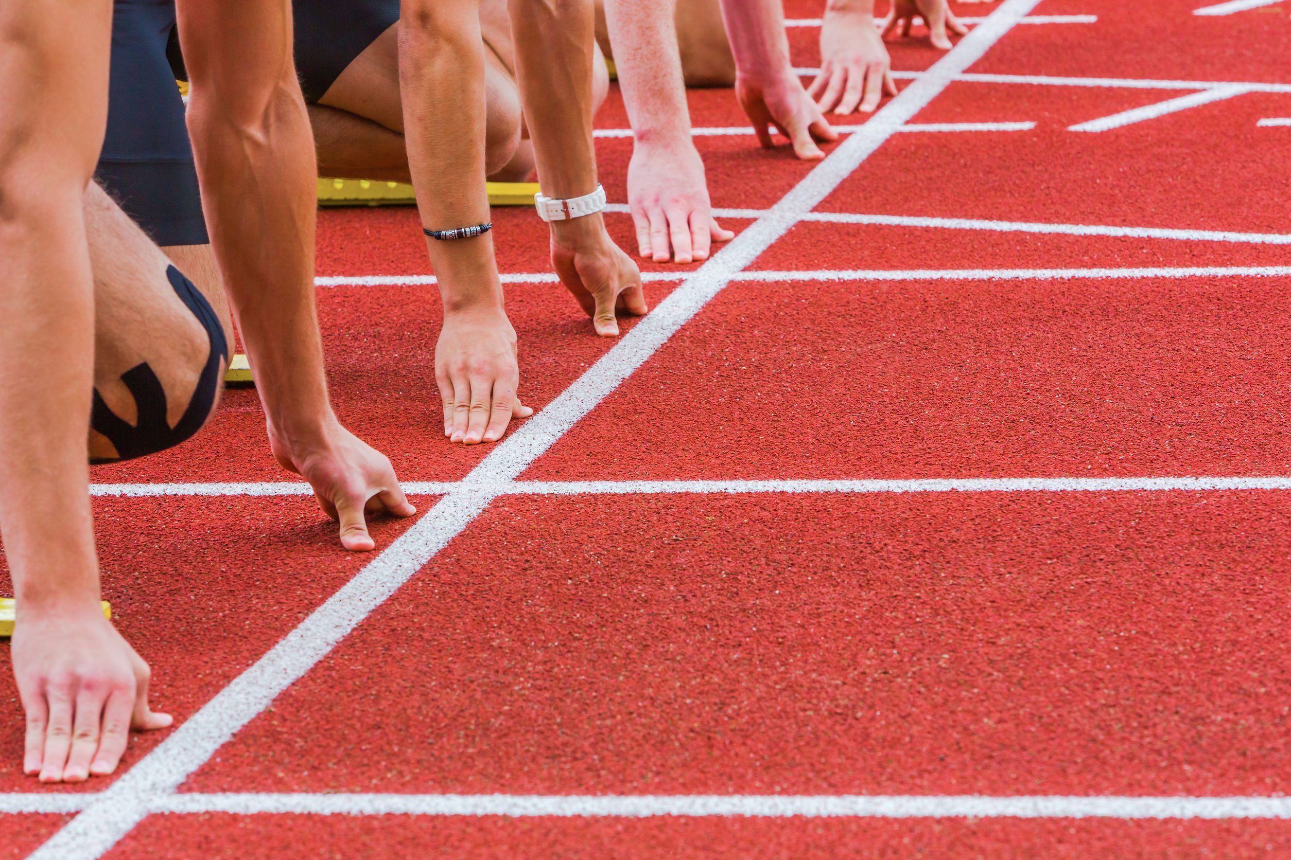 Runners' hands on the starting line of a track, ready to begin a race.