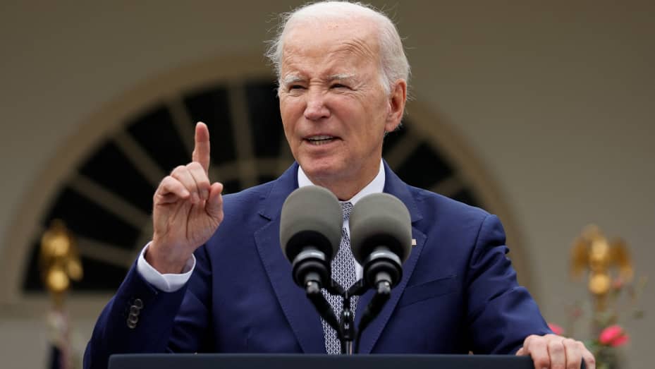A man in a suit gestures while speaking at a podium with microphones.