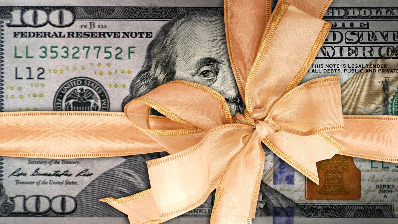 A stack of hundred-dollar bills tied with a golden ribbon and bow.